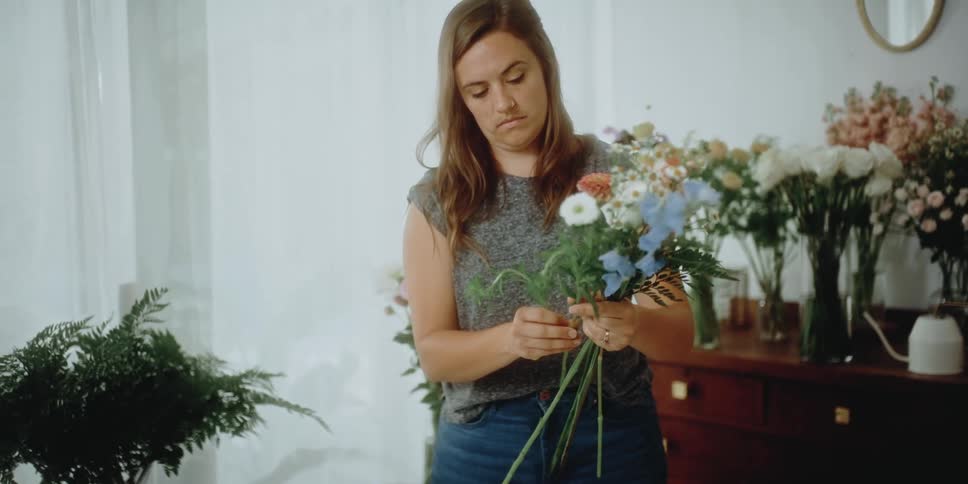 A female florist holds a variety of flowers as she prepares a floral arrangement