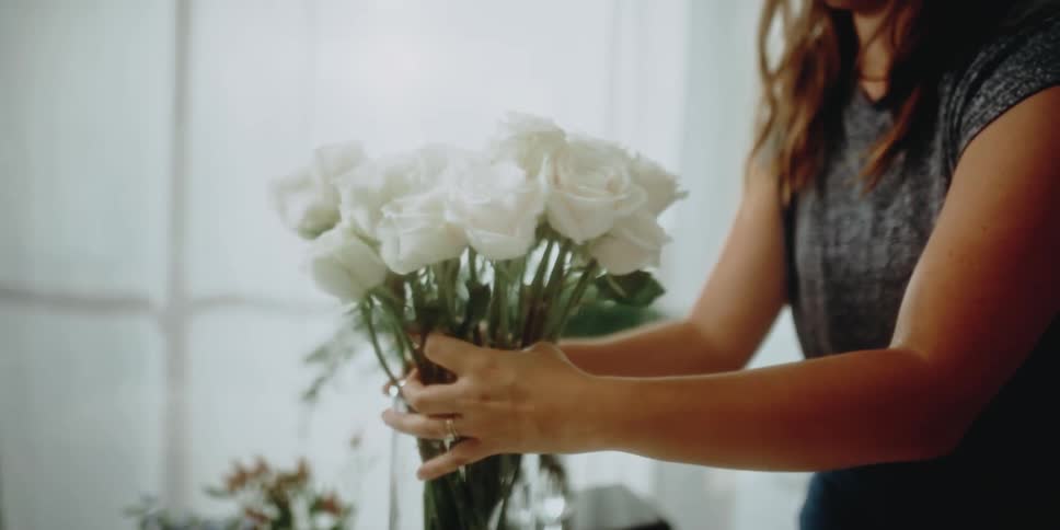A woman putting a bouquet of white roses into a glass vase indoors