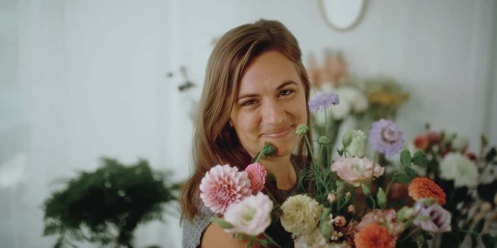 A florist poses in her store with a large bouquet of mixed blooms