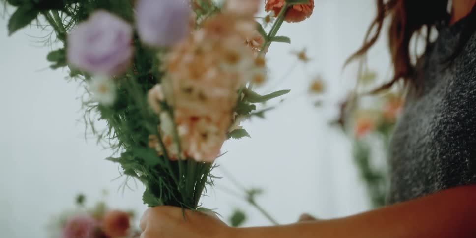 A woman in a room arranging flowers with a wall and plants in the background