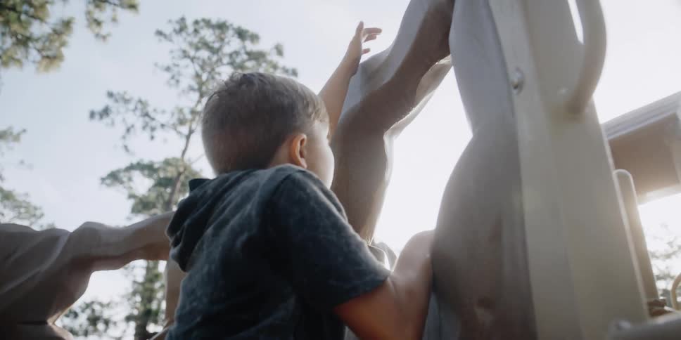 A boy climbing a rock wall on a playground in the summertime
