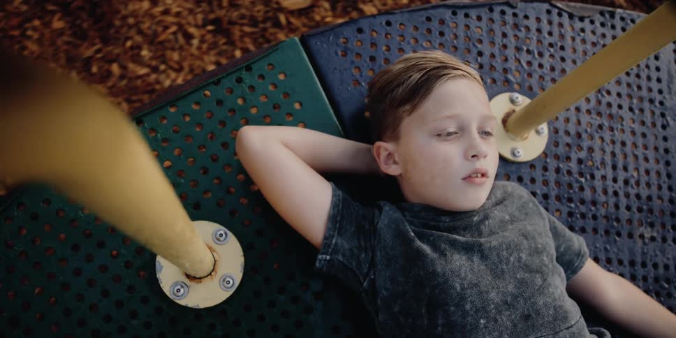 A boy lies down on a roundabout as it spins at a playground