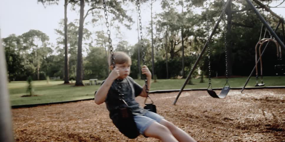 Young boy swings on a swing set in the park near the trees
