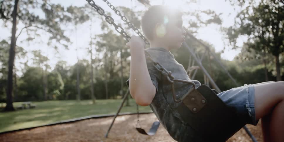 Blonde child with grey t shirt and shorts swings in the playground