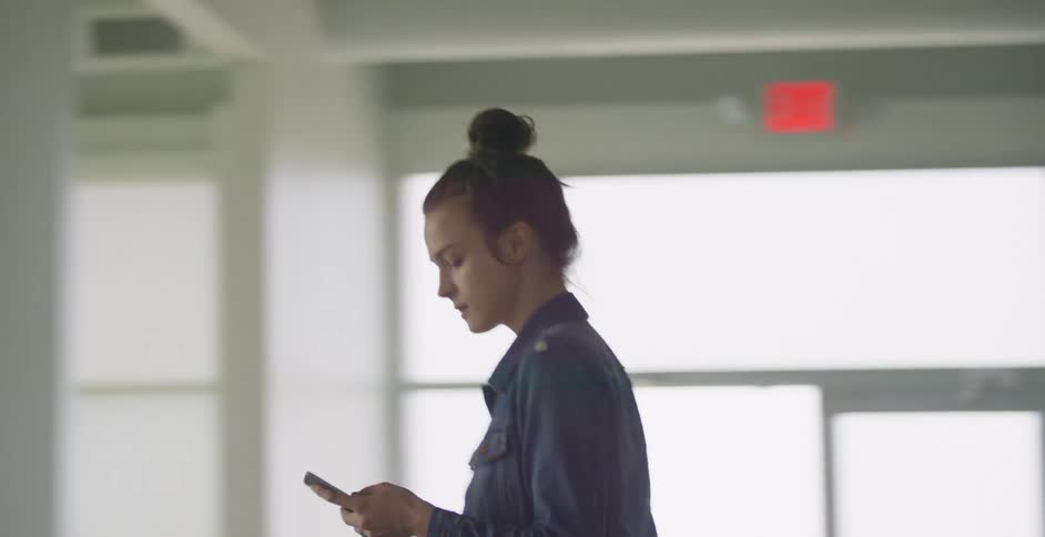 A woman walks through a hallway while looking at her phone