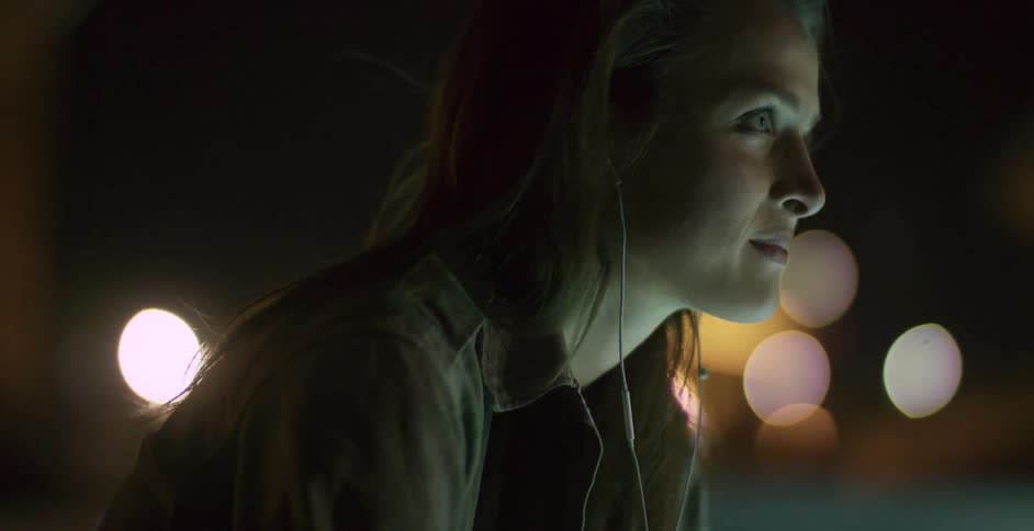 A woman wearing earbuds bobs her head slightly and grins