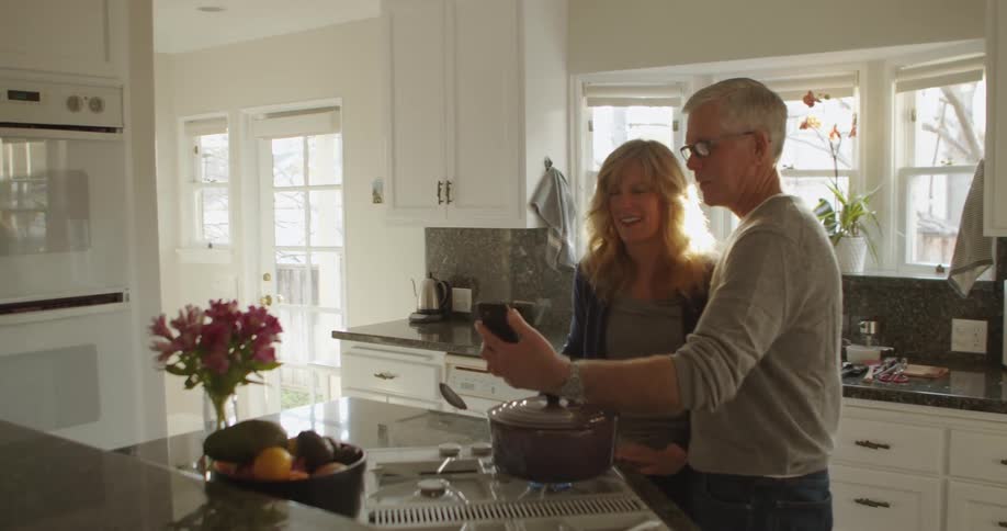 Mature couple cooking dinner at home ending a video call on a smartphone