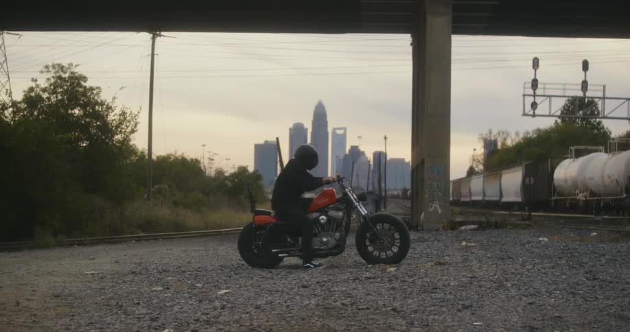 A person riding a motorcycle next to a train with the city skyline the sky and clouds in the background