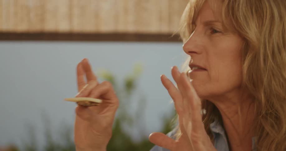 A woman sitting at the table with food and wine talks to someone