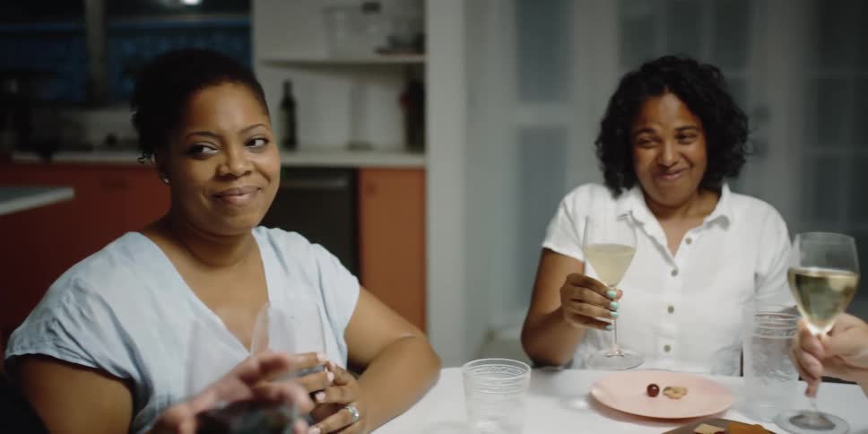 Five women sit at a table at home and give a toast to one another with wine