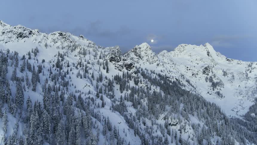 A bright full moon hangs low over a snowy mountain ridge at first light