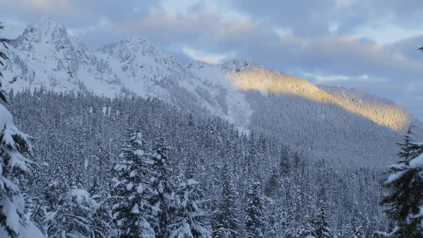 A ray of sunshine lights up a sliver of a cold and frosty snow covered mountain valley