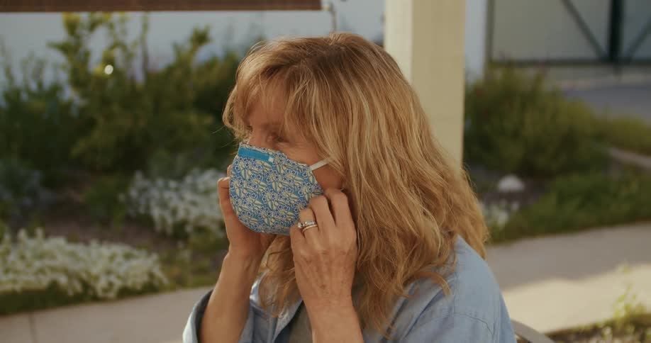 Blonde middle aged woman takes off her blue mask sitting in the garden