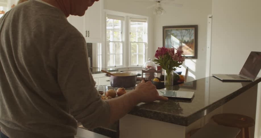 A man and a woman in a kitchen looking at a tablet with a wall in the background