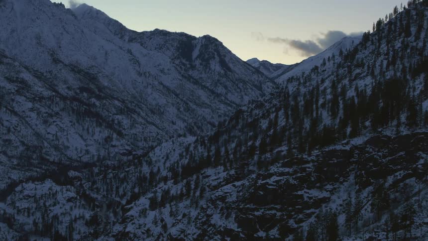 Traverse along a frigid and snow dusted mountain valley under a crisp sunset sky