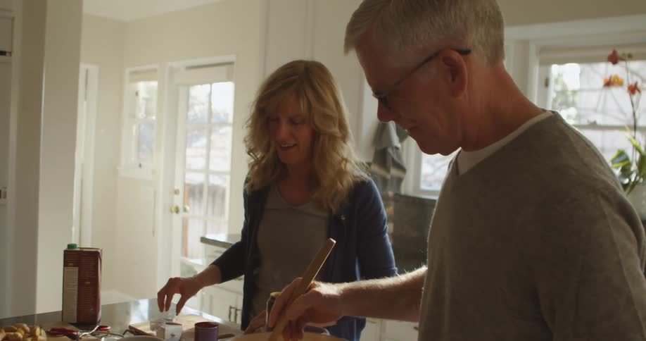 A man and a woman in a kitchen with the man stirring a pot on a stove