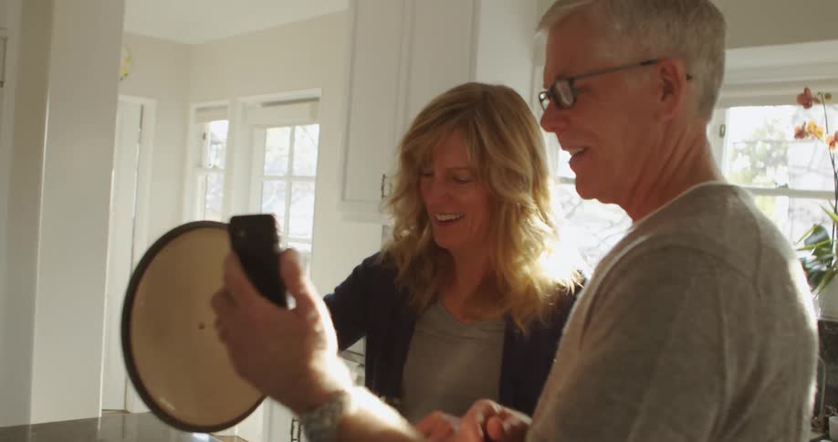 Mature couple cooking dinner at home while watching a smartphone