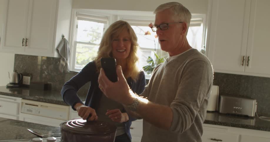 A man and woman cooking at home video chat on a cell phone and show the pot of food they are making