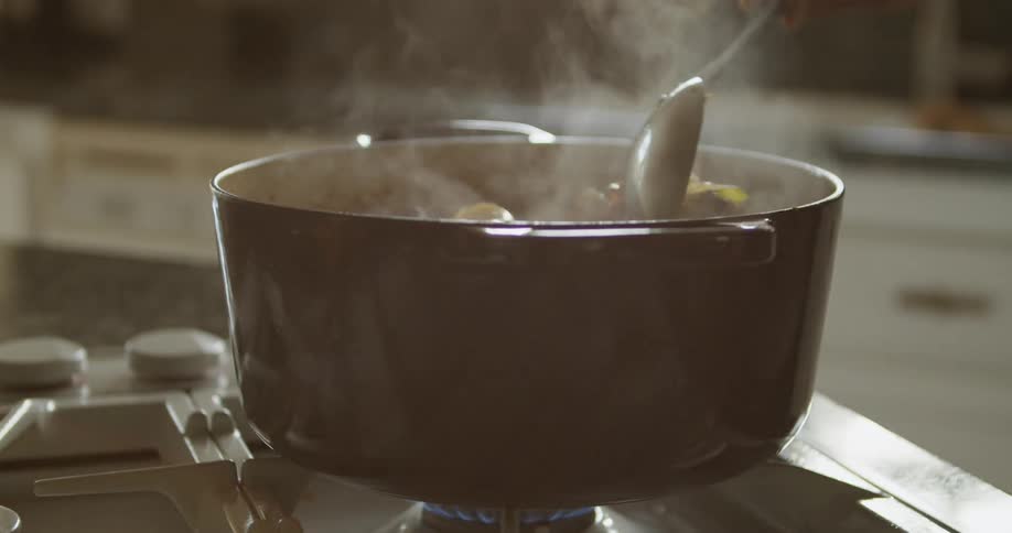 A woman cooking at home stirs a pot of food on the cook top