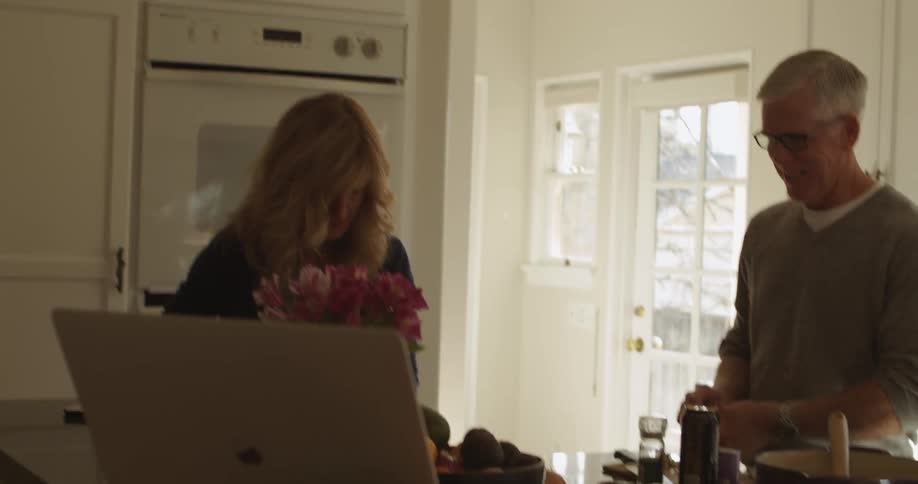 Older couple works together in kitchen laughing and smiling while viewing computer screen