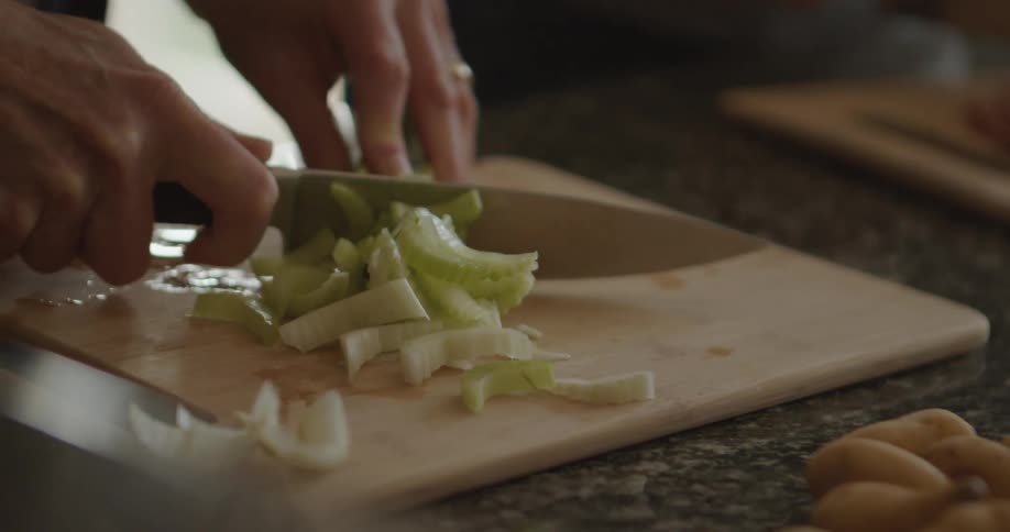 Womans hands cut celery plant on cutting board in the kitchen