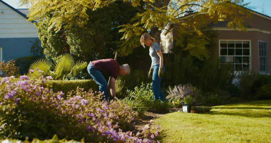 A man and a woman in the front yard working in the garden with plants