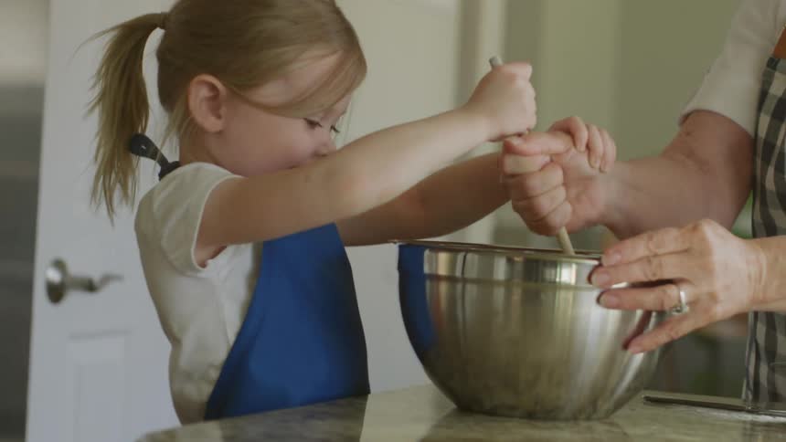 A girl and a woman in the kitchen with a wooden spoon mixing a mixing bowl