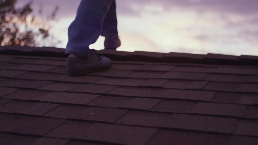 Person walks over roof as view of pink tinted sky over horizons comes into view under a cloudy sky