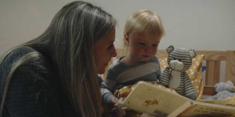 A woman reading a book to a boy in a bedroom