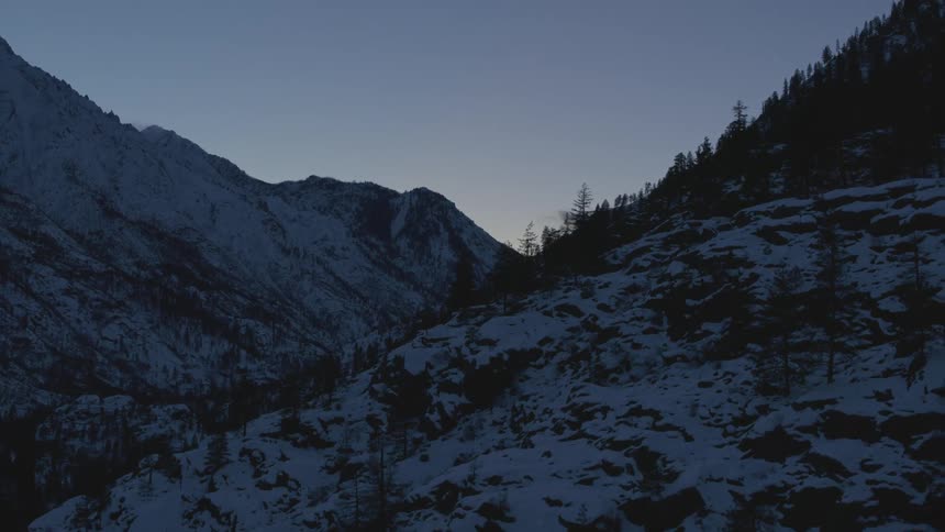 Descent into a dark and frigid mountain valley under a clear blue sky