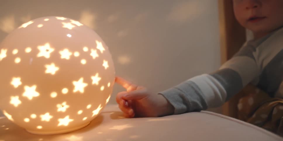 Toddler resting in bed touches a night light with his finger