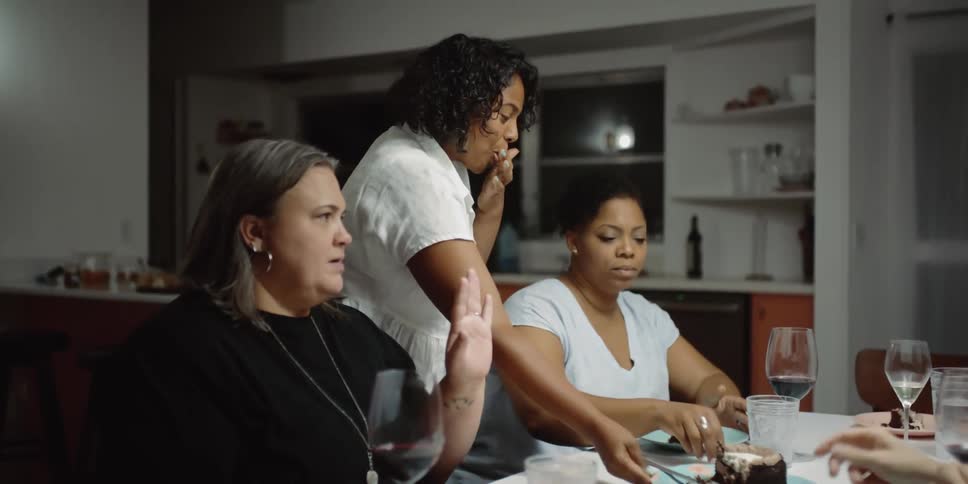 Women sitting around the table with cake with a wall and window in the background