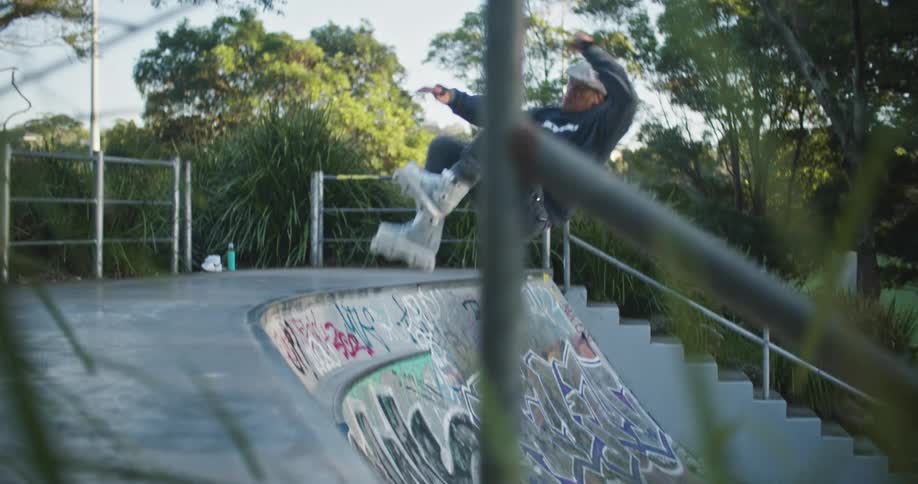 A man in a skate park skating with in line skates with trees the sky and clouds in the background