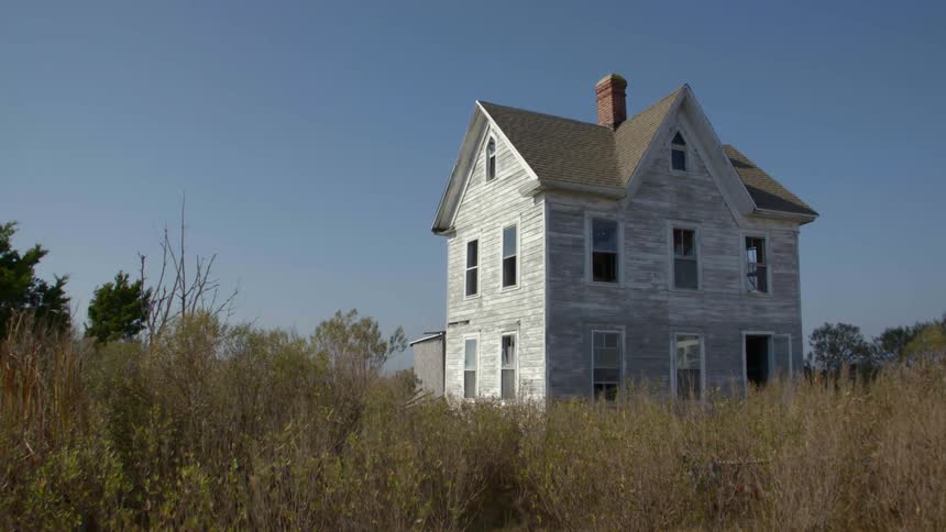 Old abandoned house with weeds and grass moving in the breeze
