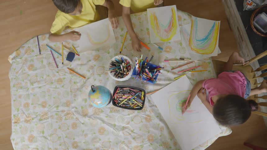 Three kids are sitting at a table and coloring pictures