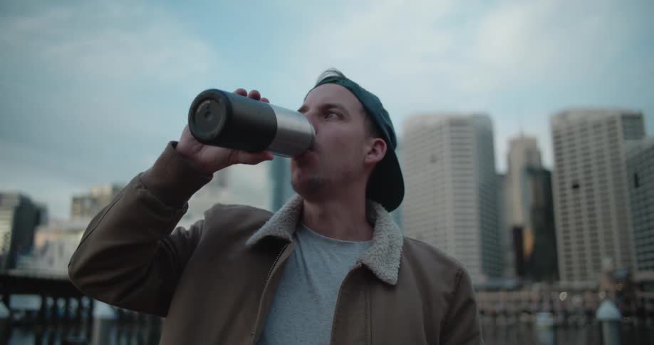 A man with his hat on backwards is drinking from a metal water bottle