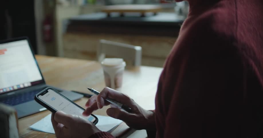 Man sitting at a desk in front of a laptop using a smartphone