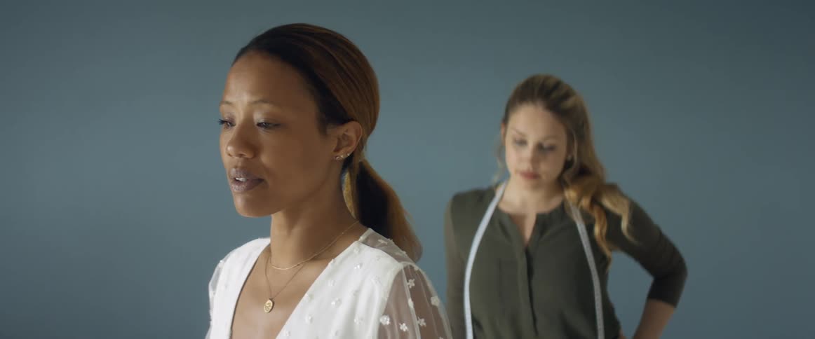 Two women in a room with one with a measuring tape with a wall in the background