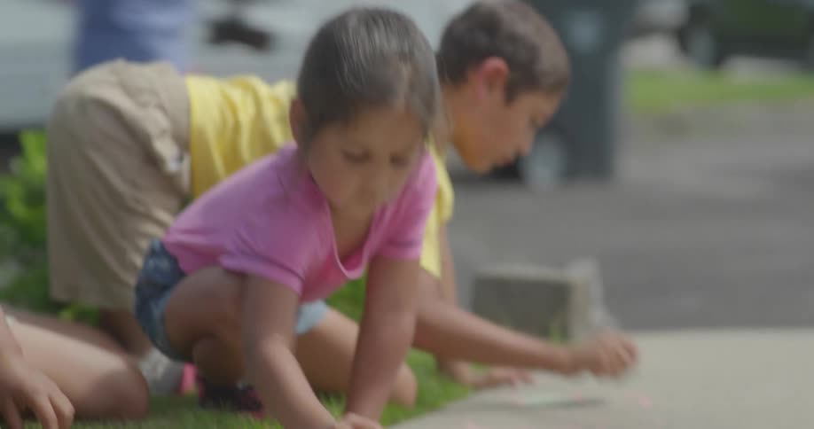 Group of children drawing with colorful chalk on the sidewalk at daytime