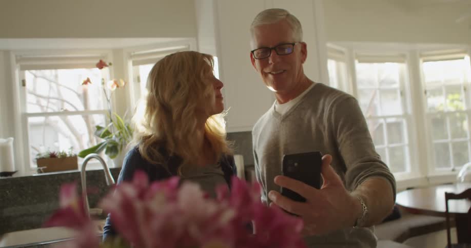 A man and wife are indoors and talking on a cell phone