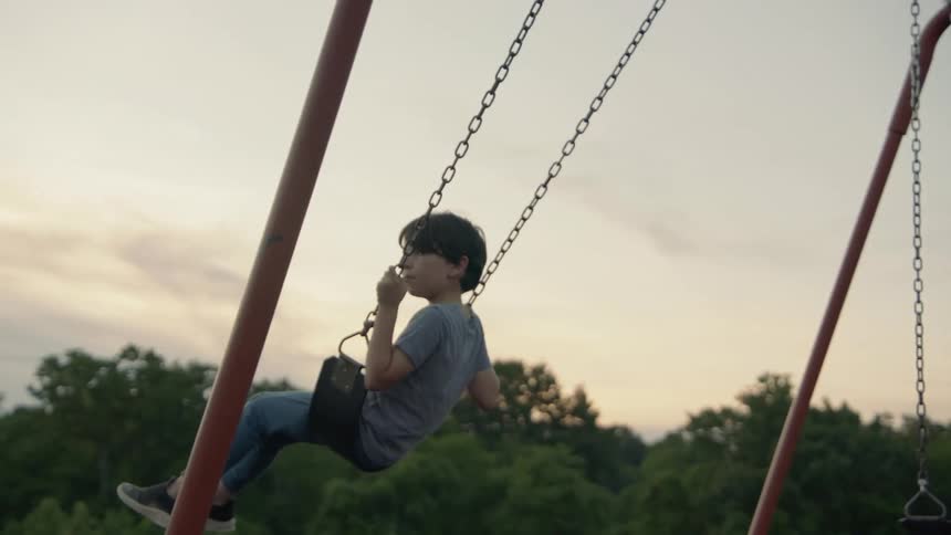 A boy swings on a swing set in a playground surrounded by trees