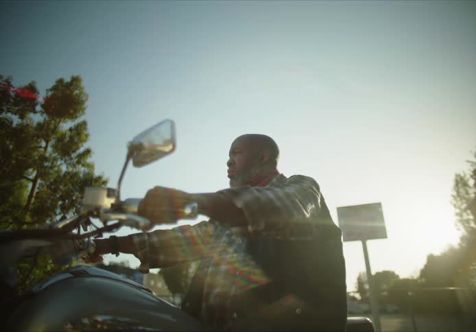Man sits on parked motorcycle looking around on a sunny day