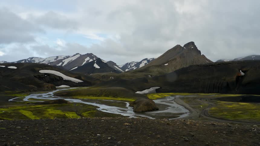 A river winds through a field in front of a mountain range