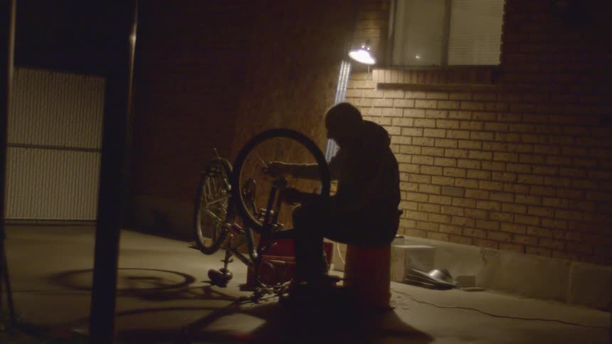 A man is fixing a bike and sitting outdoors at night