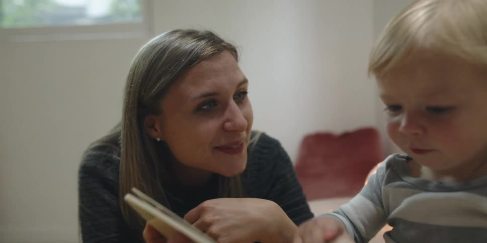 A mom smiles as her child points at a book they are reading together