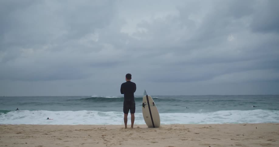 A man standing next to a surfboard on a sandy beach