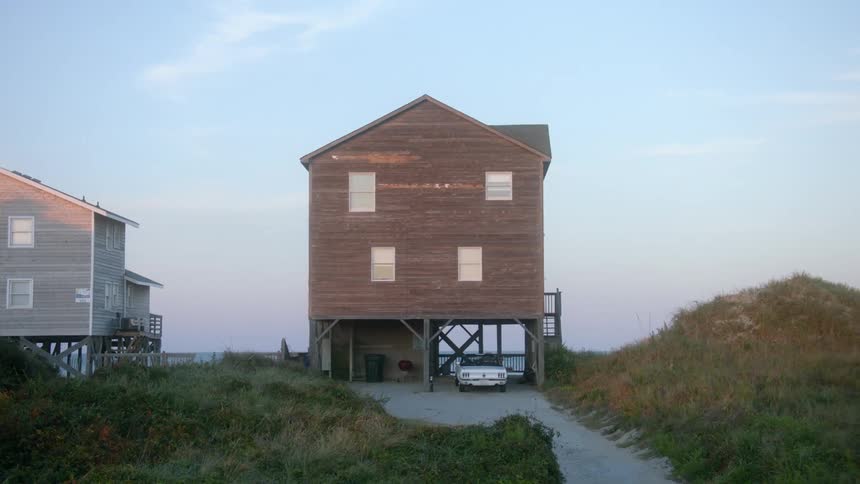 A house with a vehicle parked underneath with the sky and clouds in the background