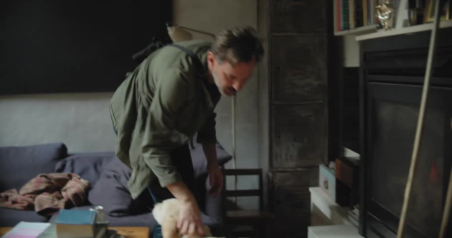 A man is walking around his house and petting his dog