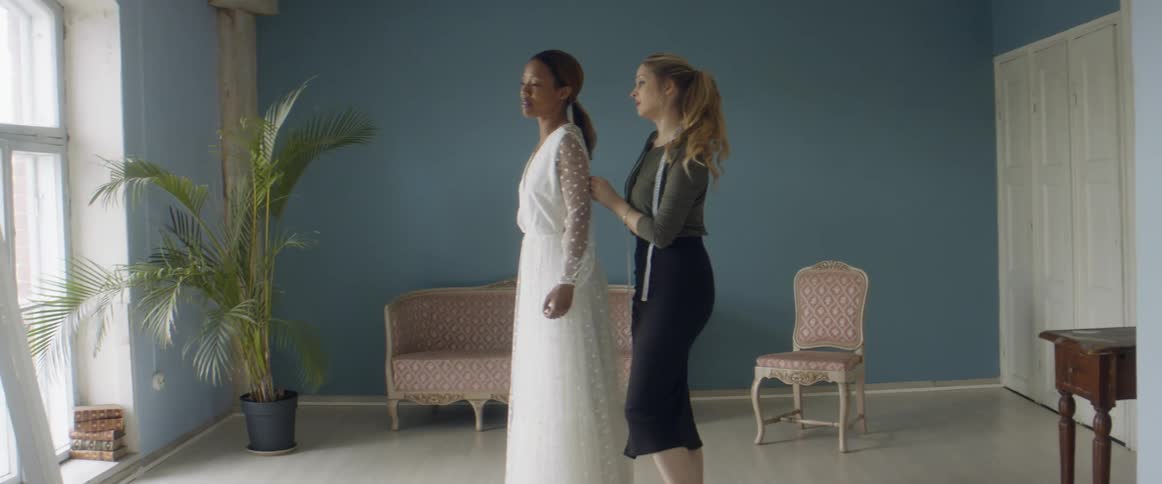 A friend is helping her friend put on a dress indoors