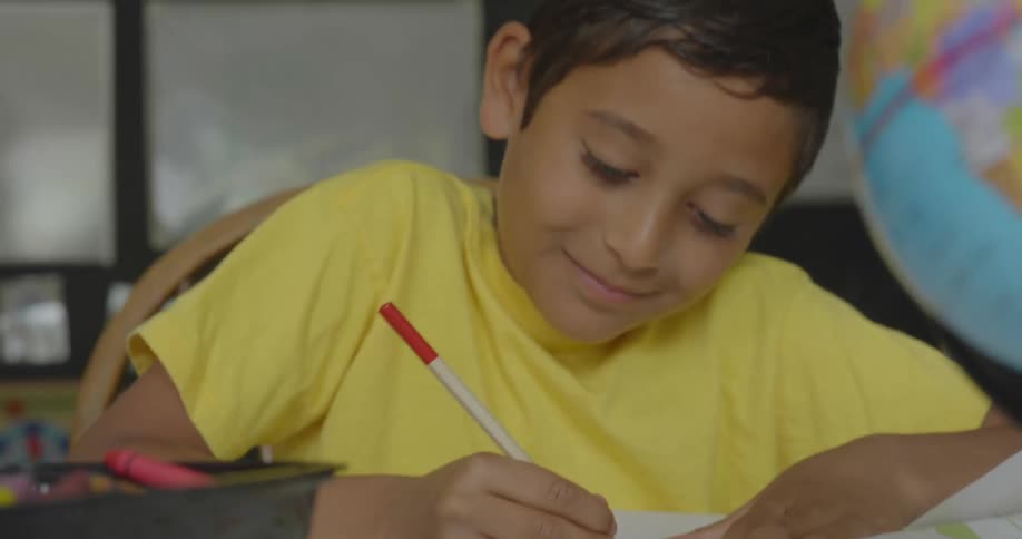 Elementary student wearing yellow shirt doing homework in front of a globe
